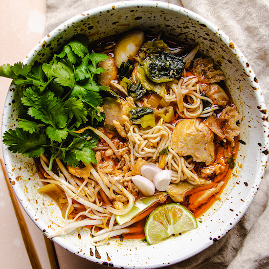 Rice noodles, chicken, cilantro, bean sprouts, sliced lime and coconut milk broth in stoneware bowl