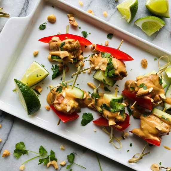 Skewers of satay chicken bites, red pepper and cucumber covered in a peanut sauce.