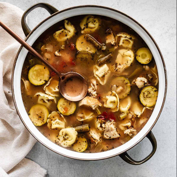 Chicken tortellini soup in a soup pot with a ladle. 