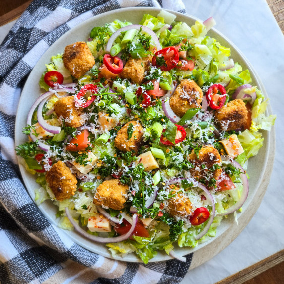 A colourful bowl of salad with pops of red, purple and green against a checkered towel
