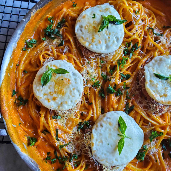 A skillet of orange, saucy bucatini & crispy patties topped with melted white mozzarella & herbs 