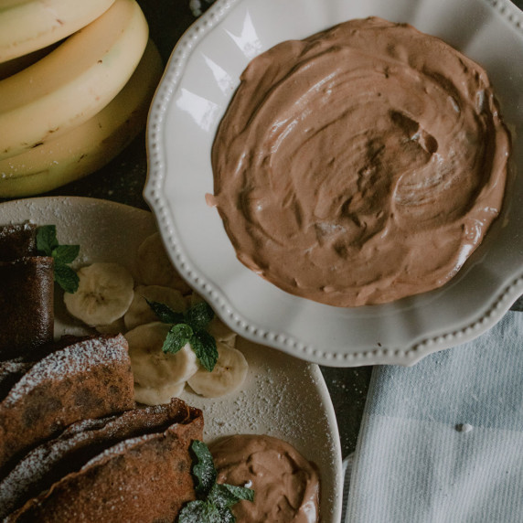 chocolate cream cheese crepe filling in a white bowl beside a plate of chocolate crepes 