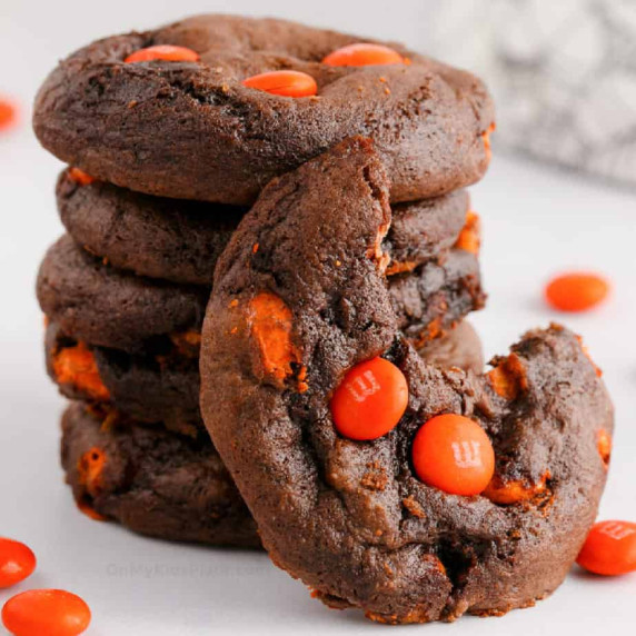 Stack of chocolate cookies with orange candies, one cookie has a bite missing.