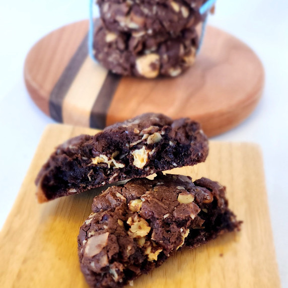 Broken chocolate cowboy cookie on a square wooden plate with a stack of cookies in the background