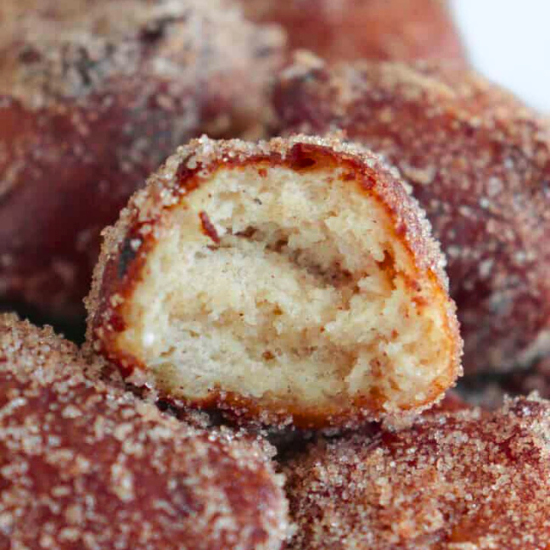 Close-up of a bite out of a cinnamon sugar donut hole, revealing its fluffy interior texture.