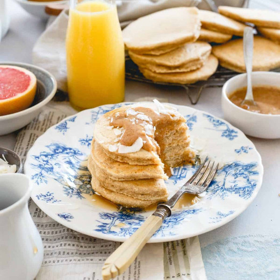 A stack of pancakes with brown sauce and coconut sits on a patterned plate.