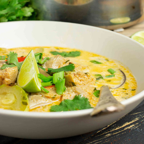 coconut curry soup in a white plate with a silver spoon