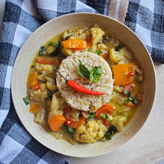 Wooden bowl full of vegetables, brown rice, and a red Thai chili with a checkered towel.