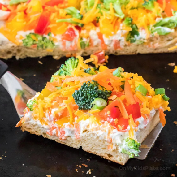 Cold veggie pizza slice on the pan at an angle being pulled away with a spatula.