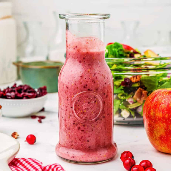 Cranberry Vinaigrette in a large glass jar from the side on a kitchen counter with salad in a bowl 