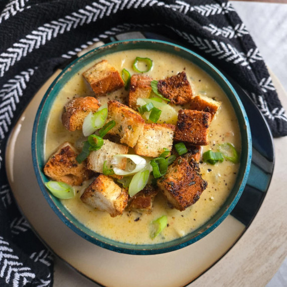 A gorgeous bowl of potato soup with golden croutons against a black towel.
