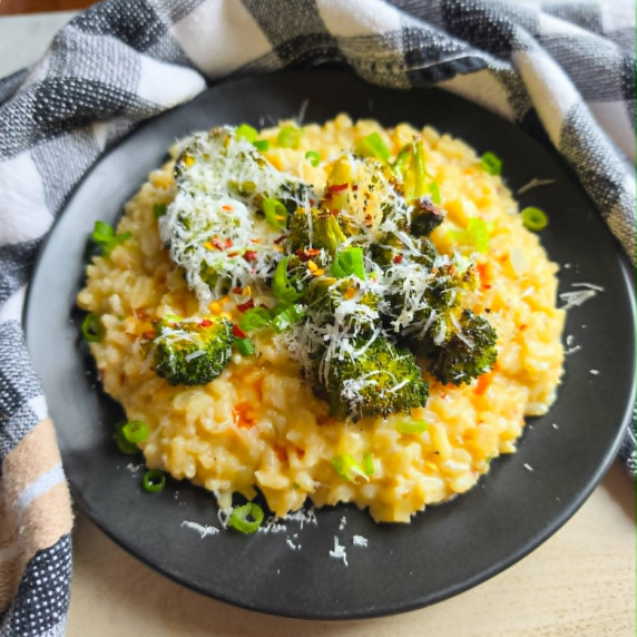 Creamy, golden risotto topped with green broccoli on a black plate.