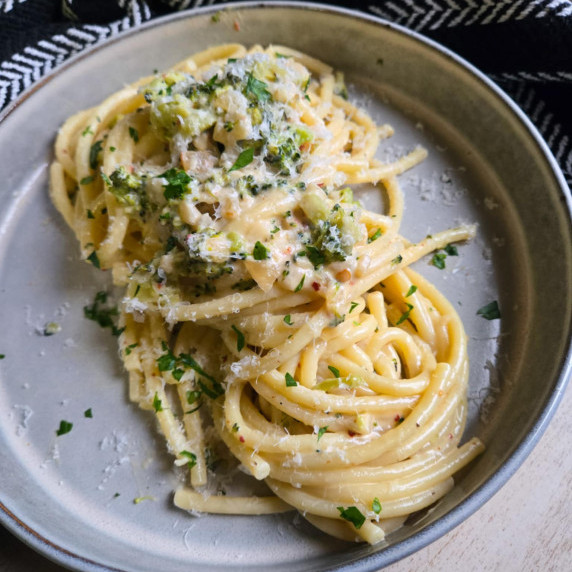 A rimmed bowl full of silky, creamy bucatini pasta with pops of green.