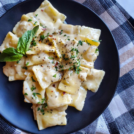 Creamy, peppery sauced ravioli on a matte black plate against a checkered cloth.