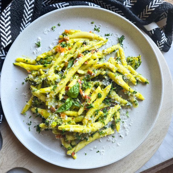 Tender noodles dressed in green pesto with green herbs on a white plate.