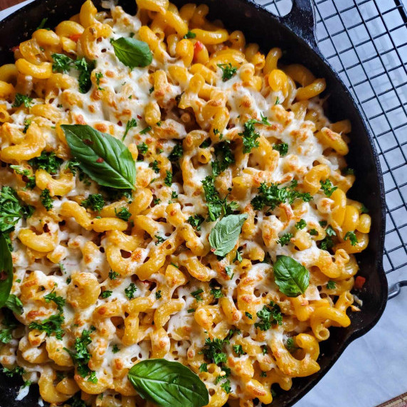 A skillet full of rosy pasta topped with fresh green herbs.