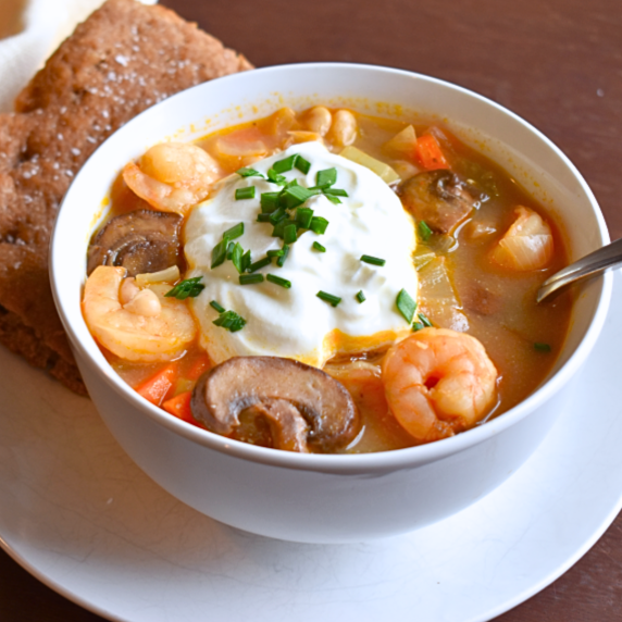 A bowl of shrimp & mushroom soup, finished with a dollop of sour cream and a sprinkle of chives