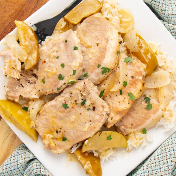 A plate of cooked pork chops with sliced onions and apples, served over a bed of white rice