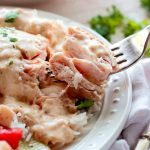 Fork full of creamy chicken, sitting on top o a bed of rice on a white plate