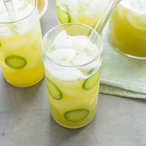 Three glasses and one pitcher of cucumber mint lemonade with cucumber slices and glass straws