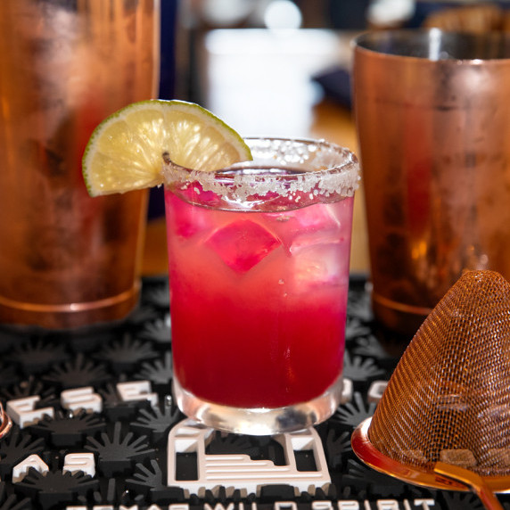 A glass of pink margarita rimmed with salt and a wedge of lime.