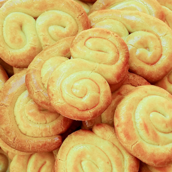 A pile of golden-brown spiral cookies with a shiny finish, stacked closely together.