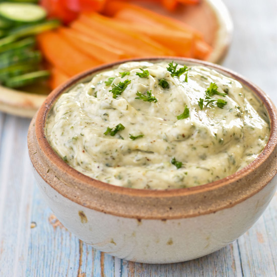 veggie dip in a pottery bowl in front of a plate of chopped veggies on a blue painted background