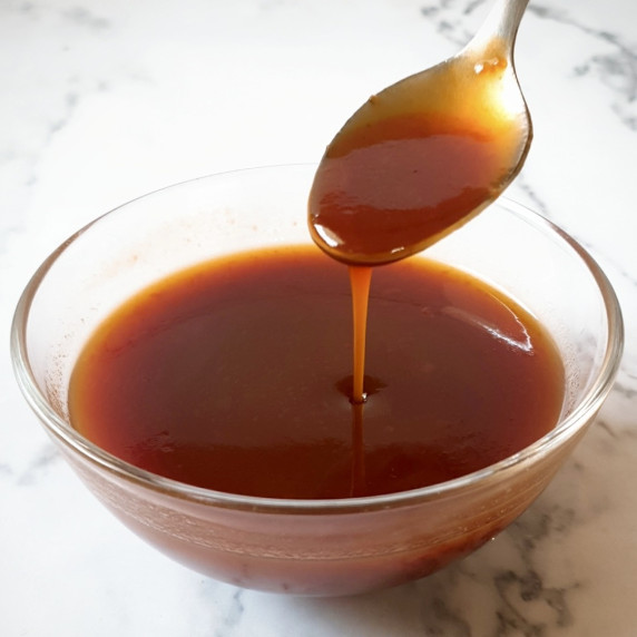Sweet and sour sauce recipe in a bowl with a spoon of it being drizzled in.