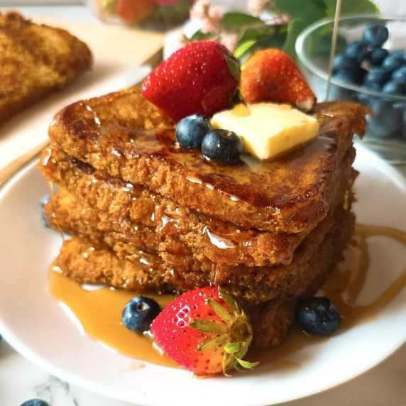 A stack of french toast drizzled with maple syrup and served with fresh fruits.