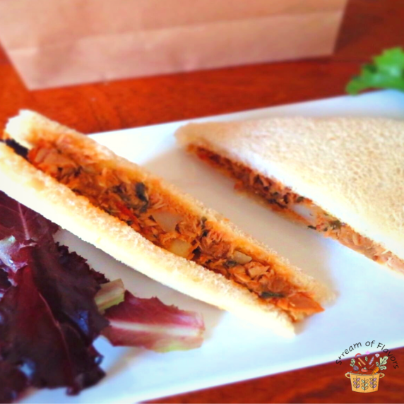 Tuna filling between white bread cut into two with some lettuce on a white plate with a paper bag