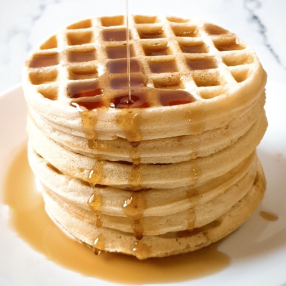 A stack of waffles with maple syrup being drizzled on top.