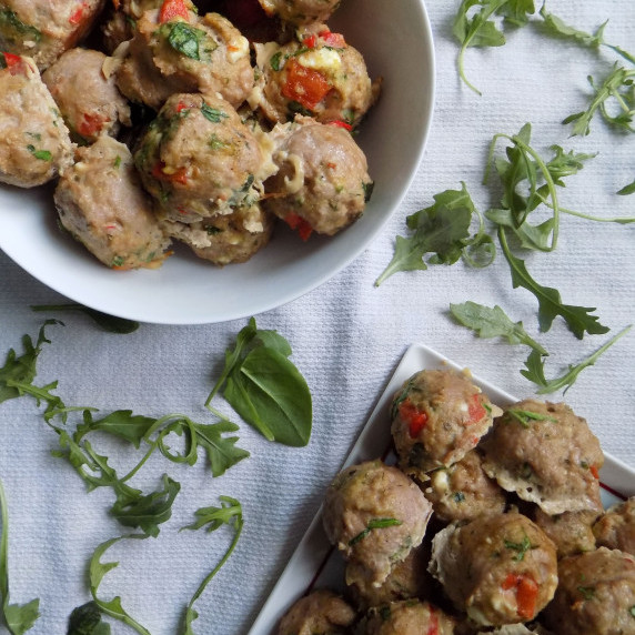 Greek turkey meatballs in a white bowl and on a white platter with scattered spinach and arugula