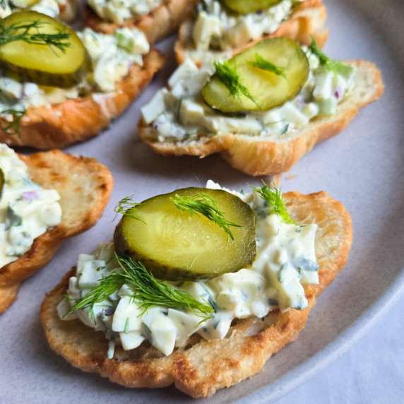 Golden croissants topped with creamy egg salad & green pickles & dill