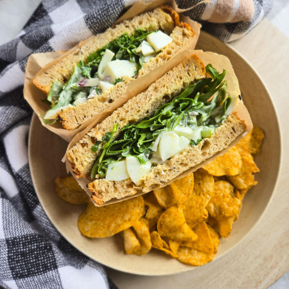 A sandwich filled with green arugula and eggs with golden chips on the side.
