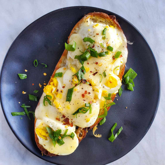 Golden brown toast topped with eggs & melty white cheddar on a black plate.