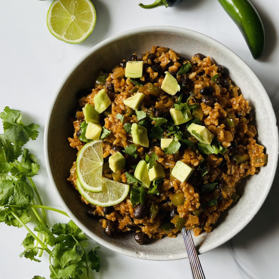 Bowl of enchilada rice topped with lime slices, cilantro and diced avocado on a marble countertop. 