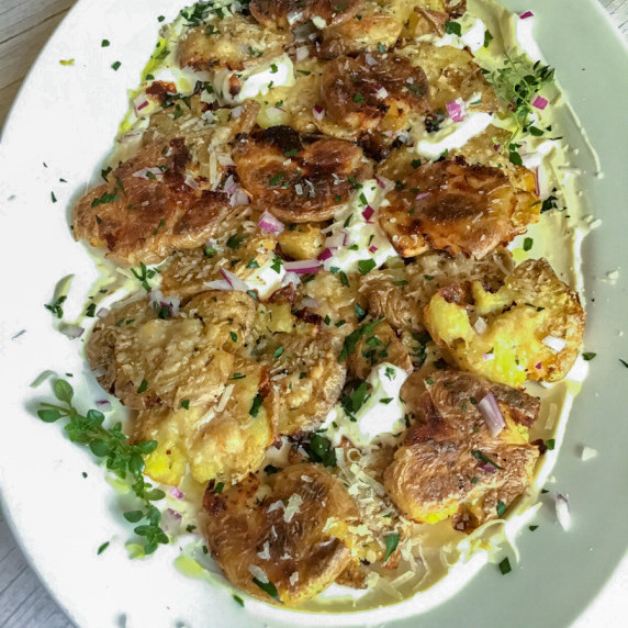 crispy smashed potatoes with parmesan on a plate with lemon whipped ricotta and fresh herbs