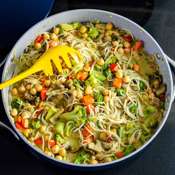 Coconut curry with rice vermicelli in a sauté pan with a pasta spoon