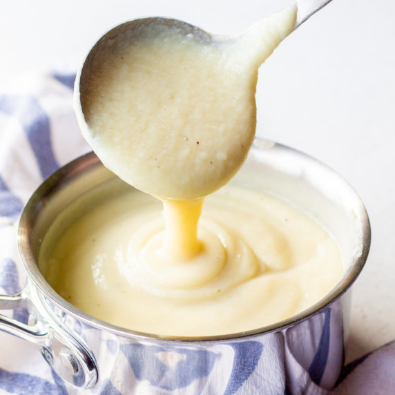 A ladle pouring creamy cauliflower alfredo sauce into a pot
