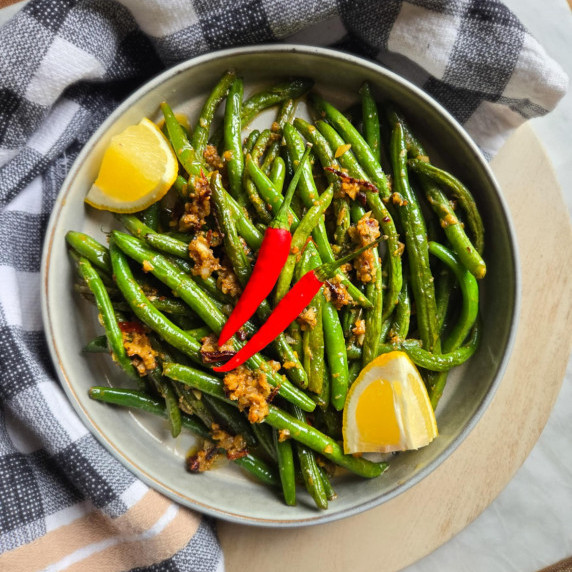 Bright green beans with yellow lemon wedges, red thai chilis, and a checkered towel.