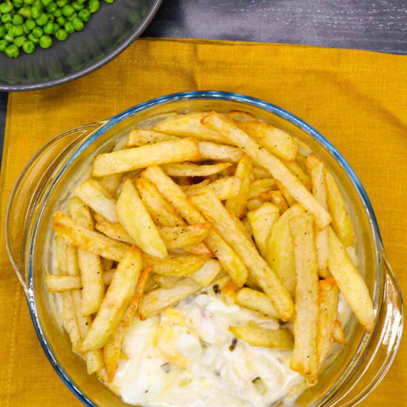 Fish pie topped with chips and peas in the background