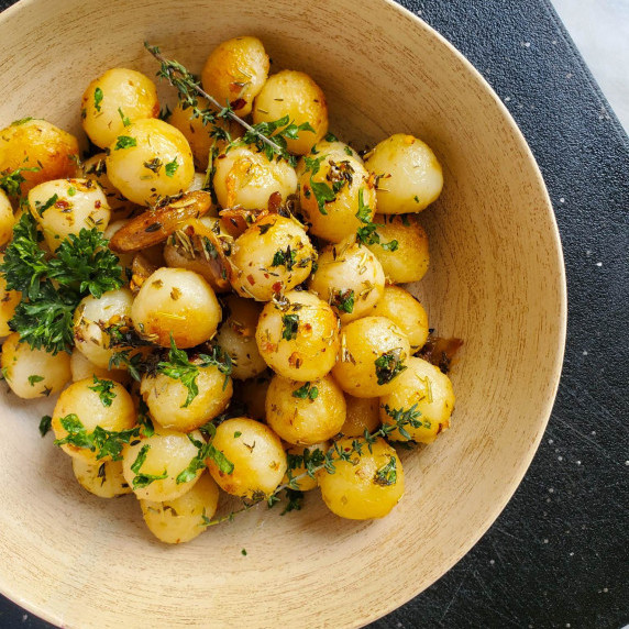 A wooden bowl of golden potatoes against a black background.