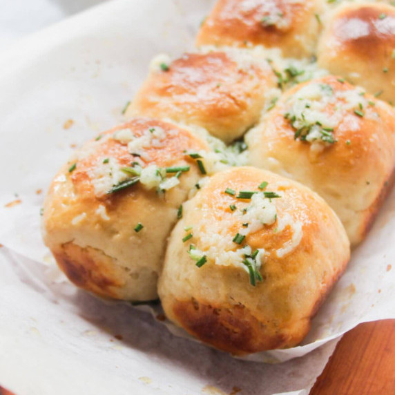 Close up of golden dinner rolls topped with a herby garlic butter on baking paper.