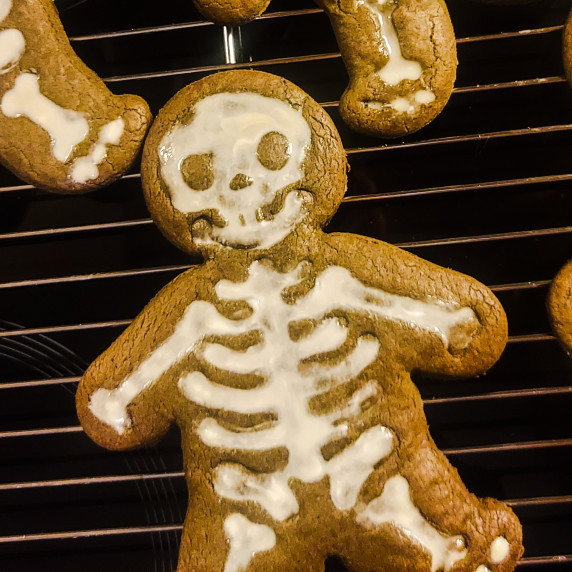 Halloween gingerbread cookie decorated like a skeleton with white icing, cooling on a wire rack.