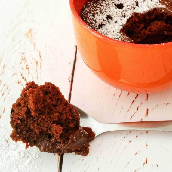 Chocolate mug cake in an orange mug with a spoonful taken out.