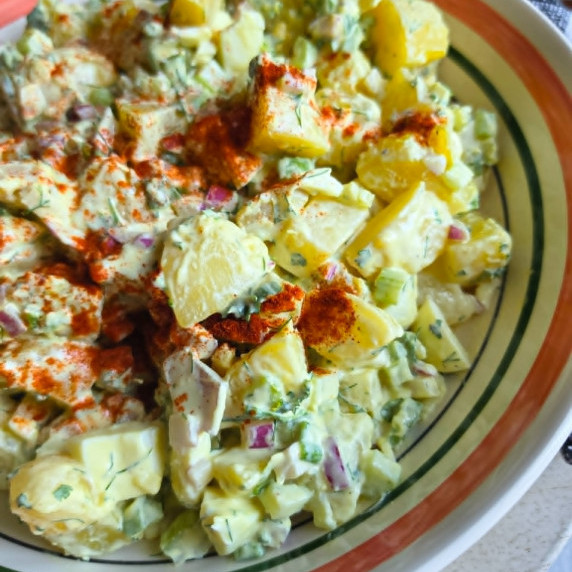 A colourful rimmed bowl full of creamy potato salad and a sprinkle of red paprika
