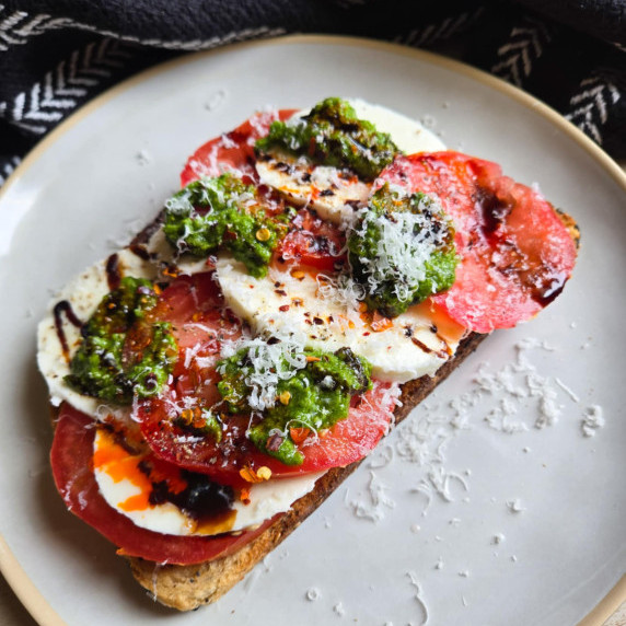 Toast topped with red tomatoes, white mozzarella, and green pesto on a white plate