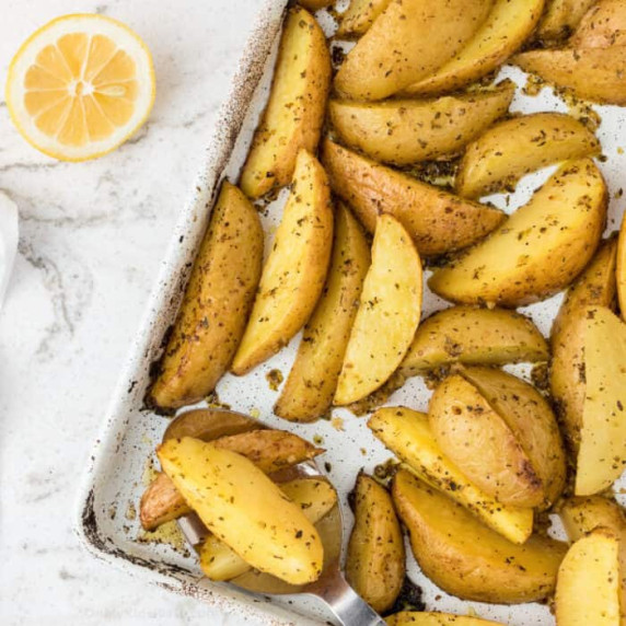Greek potatoes roasted on the pan with a lemon on the counter next to the pan.