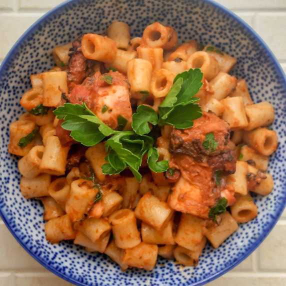 A bowl of Greek-style octopus with macaroni in tomato sauce, garnished with parsley.