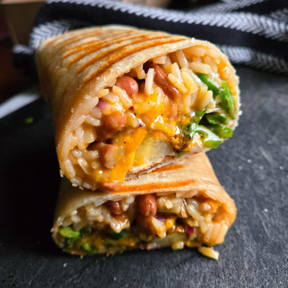 Cheesy burrito with pops of green on a black cutting board.